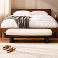 Berceau Bench seen straight on: a cream cushion held in a black lacquered wooden cradle on rounded plinth legs, at the end of a walnut bed